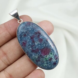 May include: Oval-shaped pendant with a silver bail. The pendant features a blue-grey stone with red and green inclusions. The stone is set in a silver bezel.