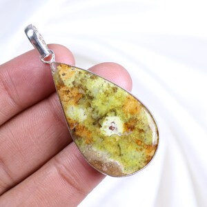 Peut inclure: Un pendentif en forme de goutte d'eau avec une bélière argentée. Le pendentif présente une pierre précieuse polie avec un mélange de teintes jaunes, vertes et orangées. La pierre est sertie dans une lunette argentée.