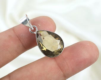May include: A teardrop-shaped pendant with a faceted, light brown gemstone. The gemstone is set in a silver-colored metal setting with a loop for a chain. The pendant is held by a person's fingers against a white background.