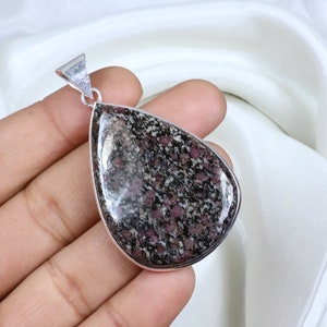 Op de afbeelding: Een druppelvormige hanger met een zilverkleurige beugel. De hanger heeft een gespikkeld patroon van donkergrijs en kastanjebruin, gezet in een zilveren rand. De steen heeft een gepolijste, glanzende afwerking.