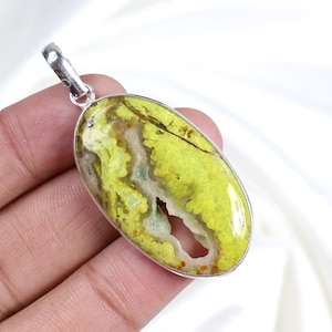 Peut inclure: Pendentif ovale avec une pierre jaune-vert vibrante, sertie dans un cadre en métal argenté. La pierre présente un motif naturel et texturé avec une cavité centrale. Le pendentif est prêt à être porté.