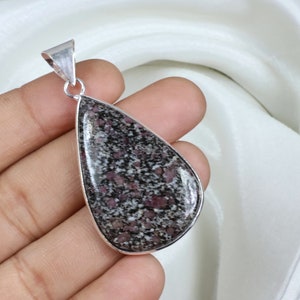 Puede incluir: Un colgante en forma de lágrima con una fianza plateada. El colgante presenta un patrón moteado de negro, blanco y rojo. La piedra está engastada en un bisel plateado.