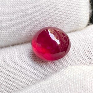 May include: A polished, round ruby gemstone in a deep red hue. The gemstone has a glossy surface, reflecting light. It is set against a white background, which highlights its colour and clarity. This image showcases a precious gemstone, suitable for jewellery.