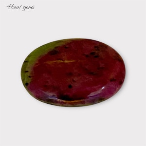 Puede incluir: Una piedra preciosa ovalada lisa con un patrón de color rojo, verde y morado. La piedra preciosa tiene un acabado brillante.