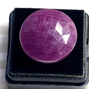 May include: A round, faceted, purple gemstone in a black velvet box.