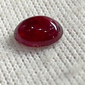 Könnte beinhalten: Ein ovaler Edelstein in tiefroter Farbe mit einer glatten, polierten Oberfläche.