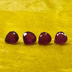 May include: Four deep red pear-shaped gemstones on a yellow surface.