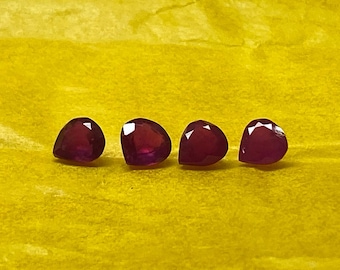 May include: Four deep red pear-shaped gemstones on a yellow surface.