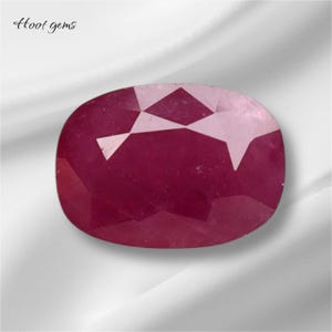 Puede incluir: Una piedra preciosa de rubí rojo intenso con un corte facetado. La piedra preciosa tiene forma ovalada y un acabado pulido.