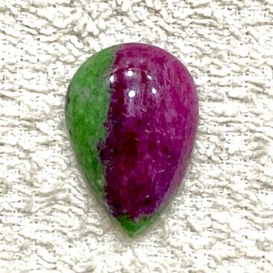Pode incluir: Uma gema cabochão em forma de lágrima com uma combinação de cores verde e rosa. A gema é lisa e polida.