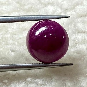 May include: A deep purple round cabochon gemstone with a smooth, polished surface.