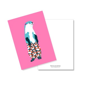Puede incluir: Una postal rosa con una nutria azul y blanca con un patrón de salvavidas rojo y blanco en su cuerpo. La postal tiene el texto "MARTHA VON MAYDELL" y "www.marthavonmaydell.com" en la esquina inferior derecha.
