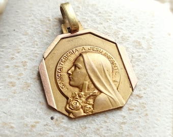 May include: Gold-toned pendant featuring a relief image of a woman with a crown of thorns and the text "SANCTA TERESIA A JESU INFANTE".