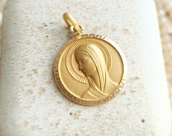 Peut inclure: Pendentif doré représentant un profil de femme en relief dans un cadre circulaire. Le pendentif a un motif de halo et est suspendu à une petite boucle. Le fond comprend des perles et de la dentelle.