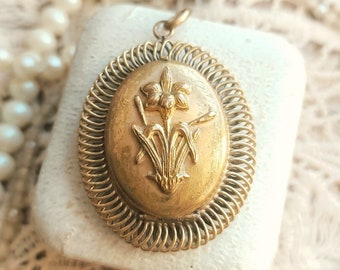May include: A gold-toned oval locket with a delicate floral design. The locket is surrounded by a decorative, coiled metal frame.