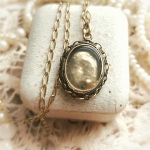 May include: A gold chain necklace with a locket pendant. The locket is oval shaped and has a filigree design around the edge. The locket is open and the inside is empty.