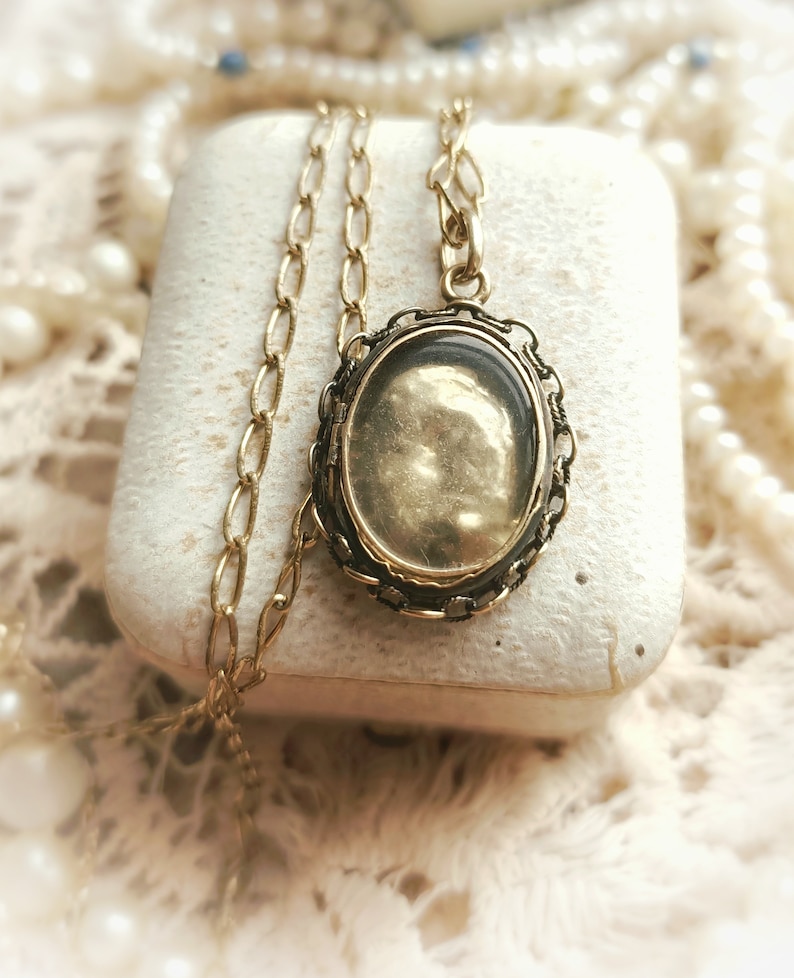 May include: A gold chain necklace with a locket pendant. The locket is oval shaped and has a filigree design around the edge. The locket is open and the inside is empty.