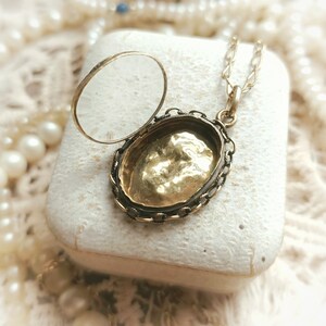 May include: A gold locket necklace with a delicate chain. The locket is open, revealing a gold interior. The locket is in a white box.