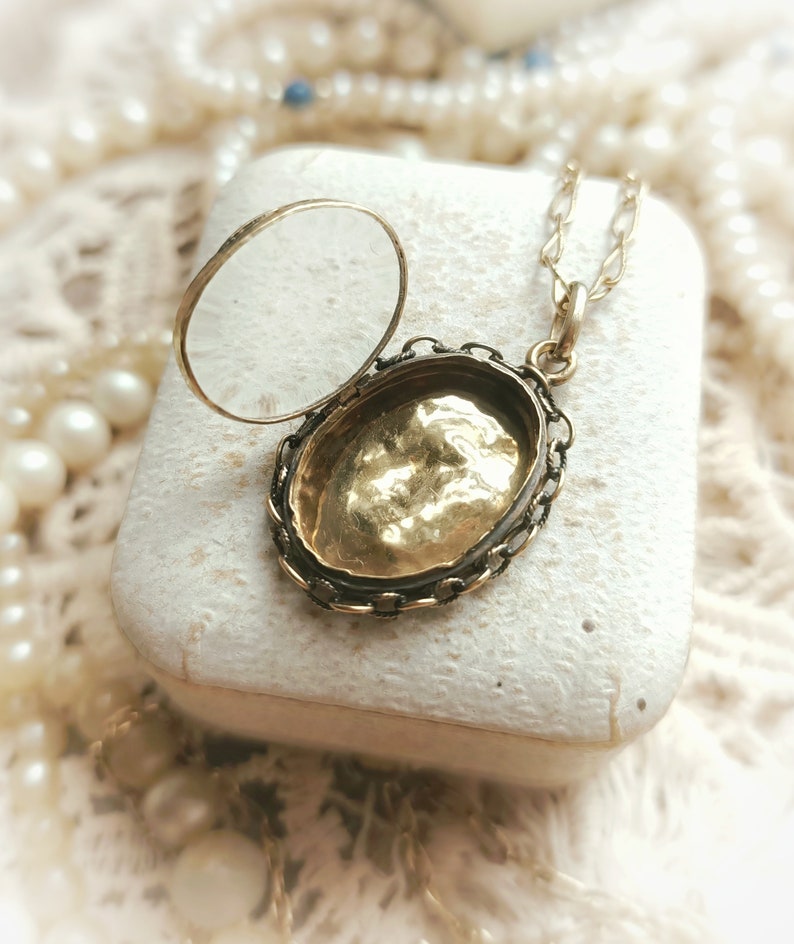 May include: A gold locket necklace with a delicate chain. The locket is open, revealing a gold interior. The locket is in a white box.