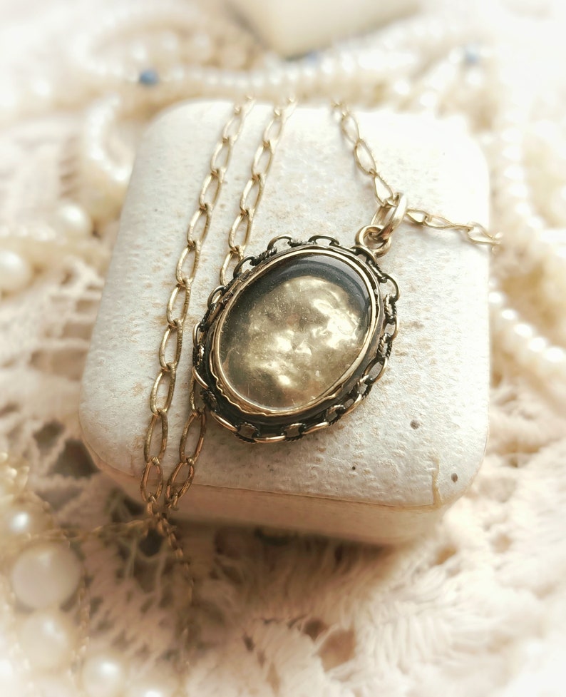 May include: A gold chain necklace with a locket pendant. The locket is oval shaped and has a gold filigree design. The locket has a clear glass front and a gold back.