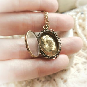 May include: A gold locket necklace with a clear glass cover and a detailed filigree design. The locket is open, revealing a gold interior.
