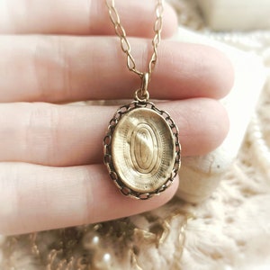 May include: A gold oval locket pendant with a delicate chain. The locket has a detailed engraved design on the front.