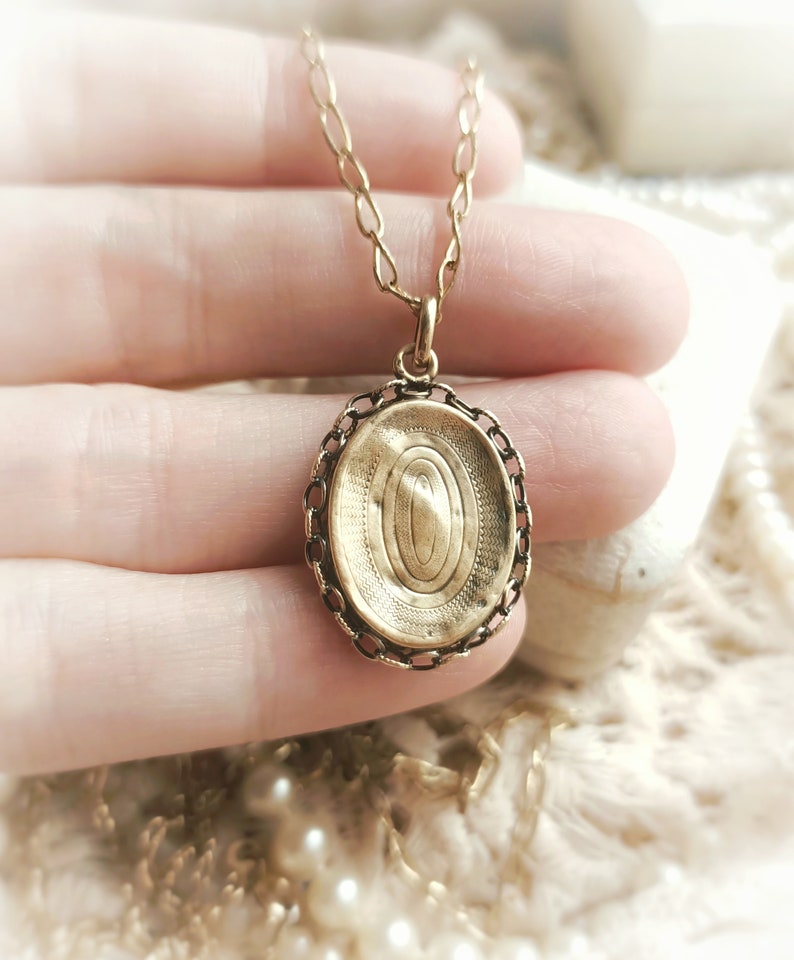 May include: A gold oval locket pendant with a delicate chain. The locket has a detailed engraved design on the front.