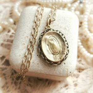 May include: A gold oval locket with a chain necklace. The locket has a detailed engraved design on the front.