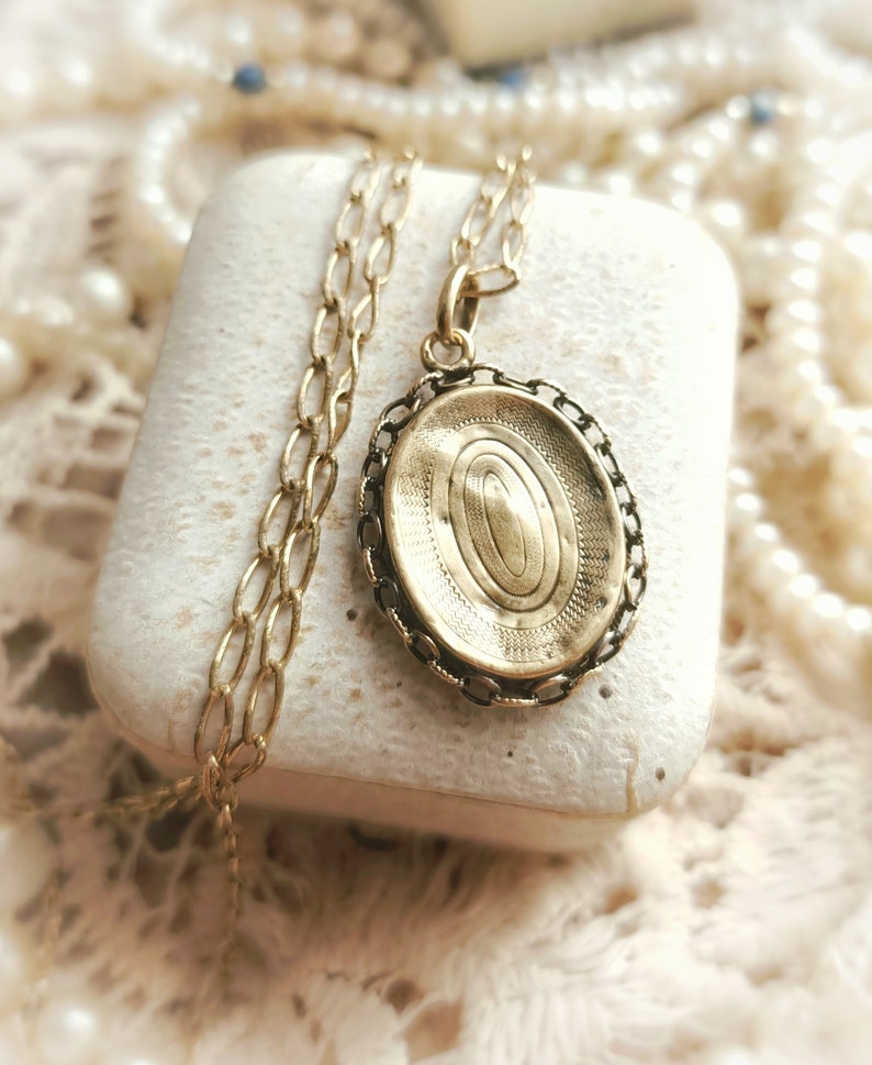 May include: A gold oval locket with a chain necklace. The locket has a detailed engraved design on the front.