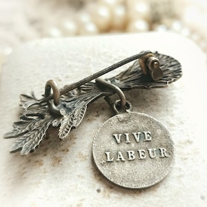 May include: A vintage bronze brooch with a floral design and a round charm that reads "VIVE LABEUR".