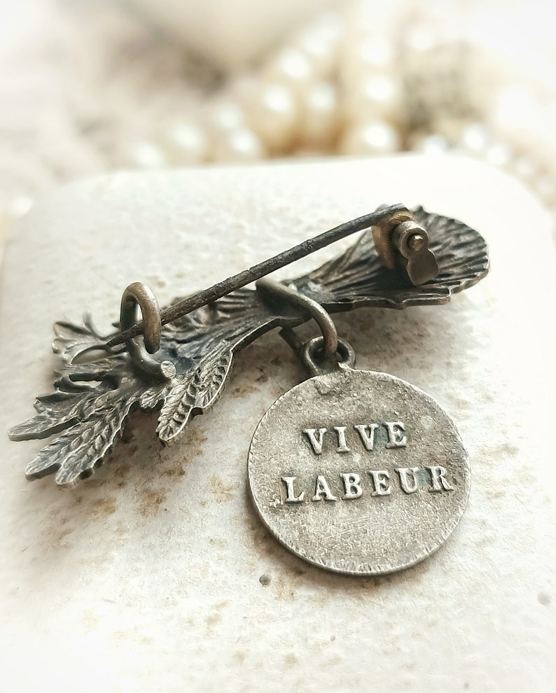 May include: A vintage bronze brooch with a floral design and a round charm that reads "VIVE LABEUR".