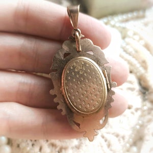 K&ouml;nnte beinhalten: Goldfarbener Anh&auml;nger mit einem verzierten, detaillierten Design. Das Medaillon hat eine Scharnier&ouml;ffnung und eine strukturierte R&uuml;ckseite.