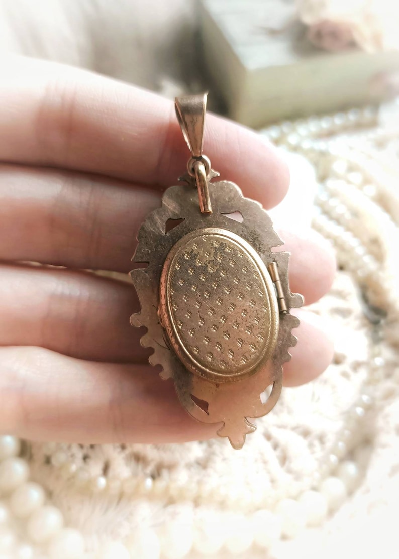 K&ouml;nnte beinhalten: Goldfarbener Anh&auml;nger mit einem verzierten, detaillierten Design. Das Medaillon hat eine Scharnier&ouml;ffnung und eine strukturierte R&uuml;ckseite.