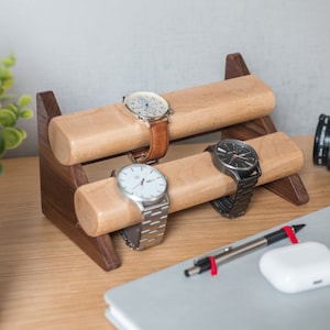 Three watches rest on a smooth maple dowel which rests on a strong walnut base. Set on a desk with notebook and camera.