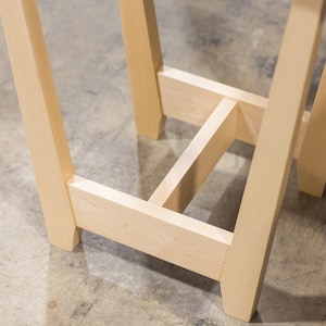 A side table placed in a living room with a plant and coffee mug sat on the table top. The side table is made from light maple hardwood and is crafted in Scandinavian minimalist modern design.