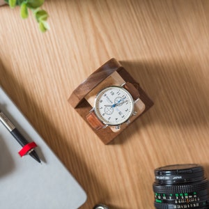 One watch rests on a smooth maple dowel which rests on a strong walnut base. Set on a desk with notebook and camera.