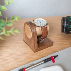 One watch rests on a smooth maple dowel which rests on a strong walnut base. Set on a desk with notebook and camera.