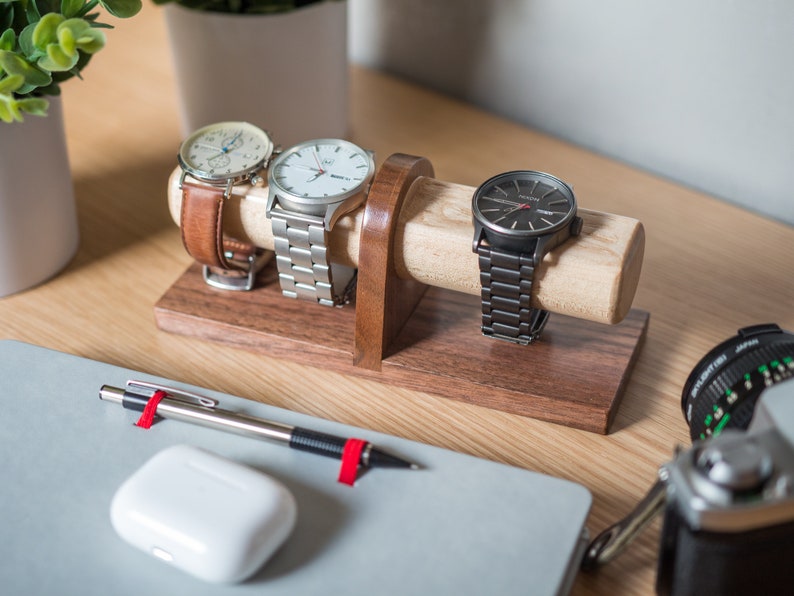 Watch display holder rests on a table, made of a long, wooden block base with one round dowel sticking out horizontally, enough space to hold four watches.