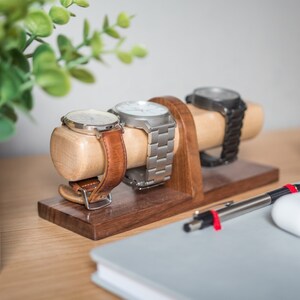 Watch display holder rests on a table, made of a long, wooden block base with one round dowel sticking out horizontally, enough space to hold four watches.