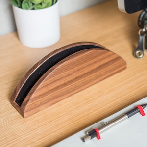 May include: A wooden phone stand with a black felt lining. The stand is shaped like a half-circle and has a natural wood finish.