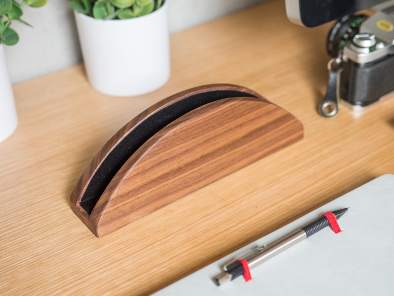 May include: A wooden phone stand with a black felt lining. The stand is shaped like a half-circle and has a natural wood finish.