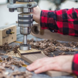 Man drills into walnut wood using a drill press.