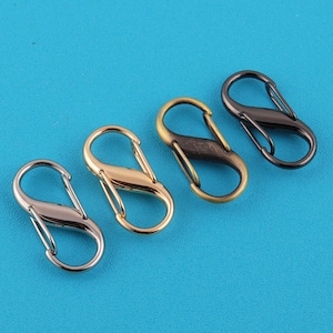 May include: Four metal spring snap hooks in silver, gold, bronze, and black, arranged diagonally on a blue background. These clasps are designed with a simple, functional S-shape, ideal for various crafting and accessory projects.