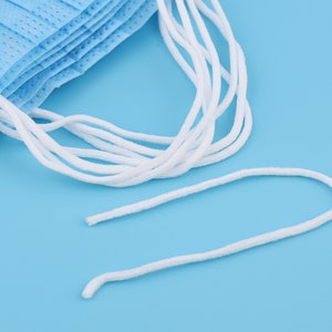 May include: A close-up of white elastic ear loops for face masks. The loops are made of a soft, stretchy material and are designed to fit comfortably over the ears.