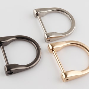 Op de afbeelding: Drie metalen D-ringen in verschillende afwerkingen: zilver, zwart en goud. De ringen zijn allemaal even groot en hebben dezelfde vorm, en ze zijn allemaal aan één kant open.