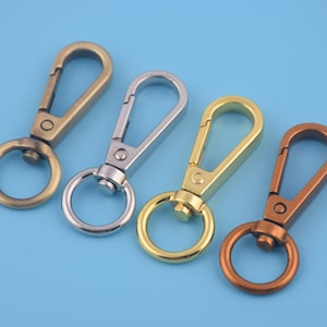 May include: Four metal keychains with swivel clips and round rings. The keychains are in antique brass, silver, gold, and copper.