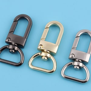 May include: Three metal swivel clasps in black, gold, and silver. The clasps are a common hardware finding for bags, purses, and other accessories.