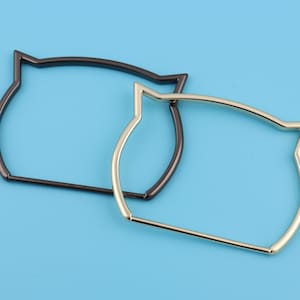 May include: Two cat-shaped metal bag handles. One is black and the other is gold.