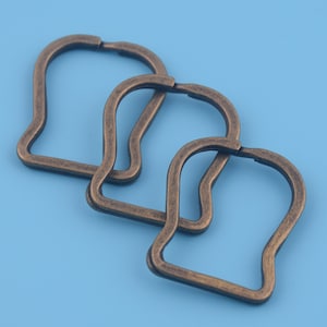 May include: Three antique gold-toned metal key rings in the shape of a heart. The key rings are linked together.