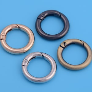 Könnte beinhalten: Vier Schlüsselringe aus Metall in verschiedenen Ausführungen: Gold, Silber, Schwarz und Bronze. Jeder Ring hat einen federbelasteten Verschluss.